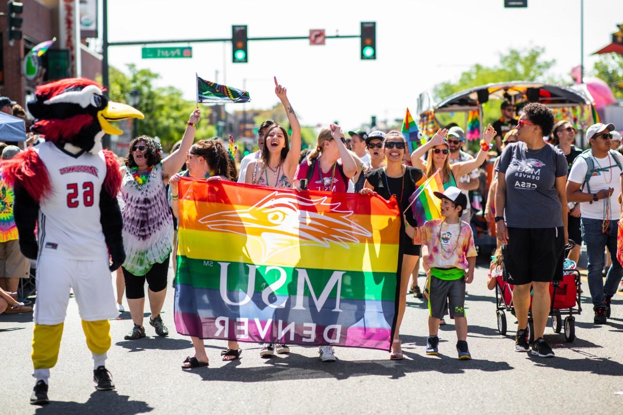 MSU Denver people in the Denver Pride Parade with a Rainbow MSU Denver flag.